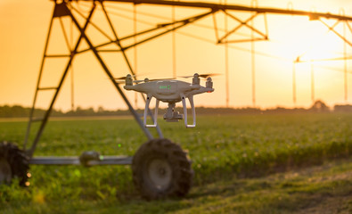 Drone flying in front of irrigation system in field at sunset