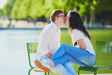 Happy romantic couple in Paris, sitting on traditional green metal chairs in Tuileries garden