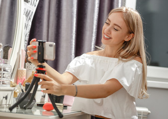 Pretty girl blogger sets the phone on the stand on the dressing table for shooting video for her...