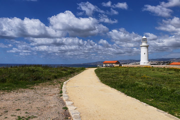 Scenery of Paphos city and nature. White lighthouse with old sand road. Pafos lighthouse for protection. Cypriot nature in spring. Sky with clouds. Traditional system for seaside cities