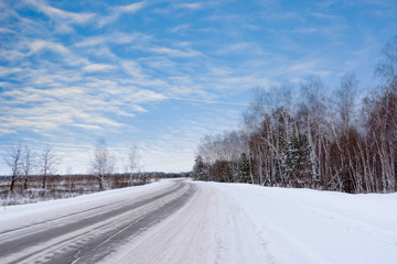Obraz premium Patterns on the winter highway in the form of four straight lines. Snowy road on the background of snow-covered forest. Winter landscape.