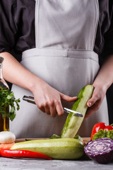 young woman in gray apron peeling cucumber
