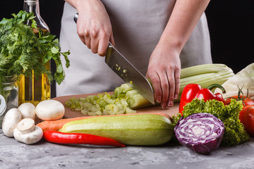 young woman in a gray apron cuts a celery