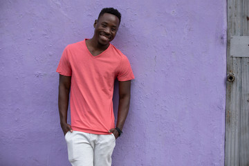 Obraz na płótnie Canvas Smiling African American man model posing in empty living coral color t-shirt standing against violet wall background