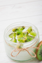 Yogurt with kiwi slices on a wooden white background.