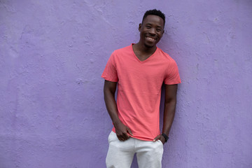 Smiling African American man model posing in empty living coral color t-shirt standing against violet wall background