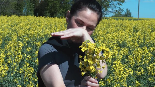 Woman on yellow canola field blowing her nose and suffering from pollen allergy