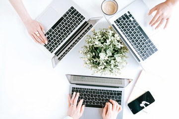 Top view on laptop with women's hands on it. Three women with laptops in office.