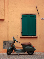 an old Italian scooter parked in front of a colorful house