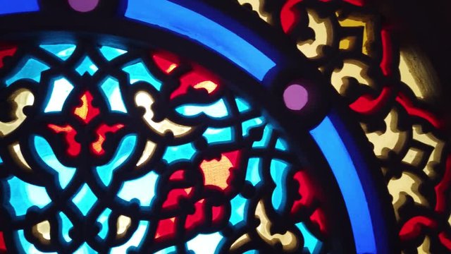 Camera pans on contemporary, abstract stained glass window in a chapel or church as sunlight streams through it 