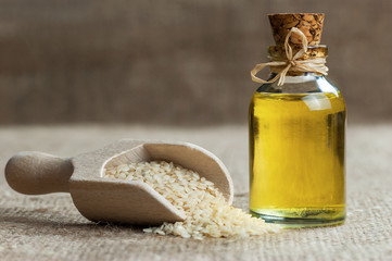 Glass bottle of sesame oil and raw sesame seeds in wooden shovel or spoon on burlap sack. Uncooked sesame background concept with copy space