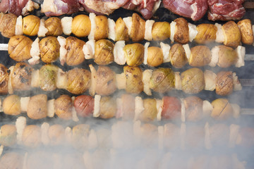Preparation of shish kebab on skewers, close-up. BBQ grill with lamb meat and potatoes