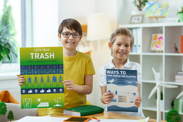 Proud joyful little boys showing informative posters about principles