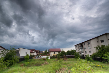Green grass and houses under dark sky with clouds before storm