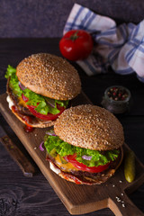 Two delicious homemade beef burgers with bacon on wooden chopping board
