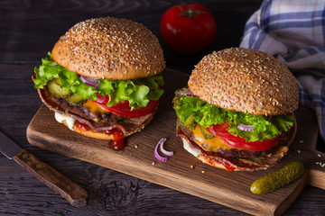Two delicious homemade beef burgers with bacon on wooden chopping board