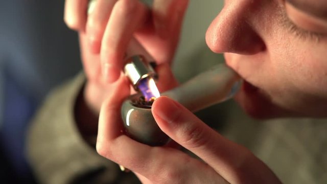 Slow motion smoking cannabis through a glass tube. Soft drug use by young people.