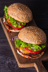 Two delicious homemade beef burgers with bacon on wooden chopping board