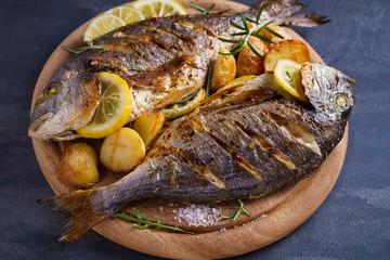 Roasted fish and potatoes, served on wooden tray - image