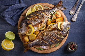 Roasted fish and potatoes, served on wooden tray. overhead, horizontal - image