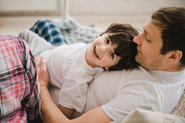 Handsome man and his son. Father's day. Father and son in their pajamas are sitting in a bed. Happy father with son playing at home on the bed, happy time.