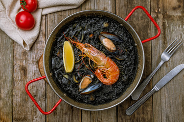 black paella with seafood on wooden background