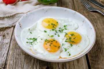 Fried eggs with tomatoes on wooden background