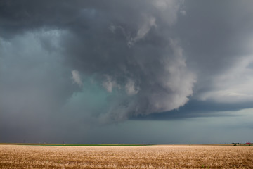 A severe supercell storm containing rain, hail, and damaging winds approaches over farmland.