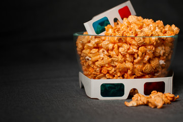3D glasses and cheesy popcorn lie in a glass plate on a gray bed