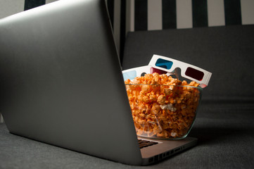 3D glasses, popcorn and a laptop are lying on the sofa in the room at night