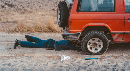 man lies under a 4x4 car on a dirt road © teksomolika