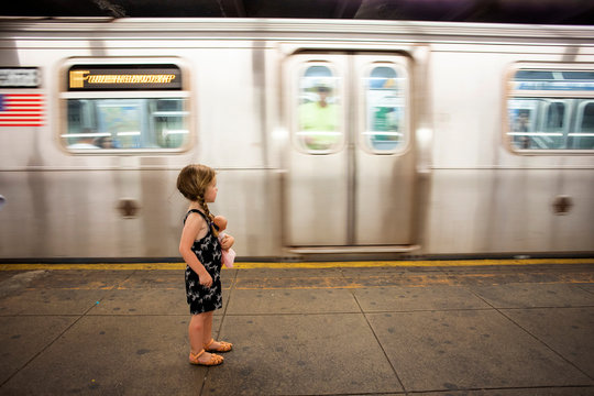 A toddler aged girl standing on the subway platform in New York City.