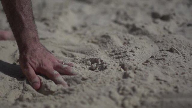 Close up shot on a man hand touching the sand beach, playing with sand or erasing memories. Slow motion concept real life visuals.