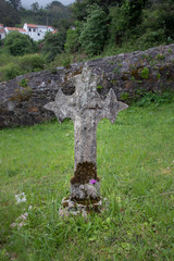Ancient stone cross of a gravestone in a rural cemetery full of grass in Galicia, Spain.