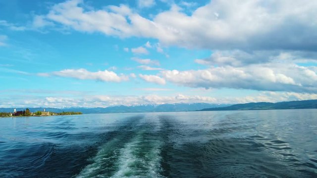 4K video of ship on Lake Constance, Bodensee. Boat sail on the lake. The water is crystal blue and behind it stands high snowy Alps. There are clouds on the blue sky.