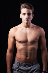 Studio portrait of handsome muscular shirtless young man isolated on black