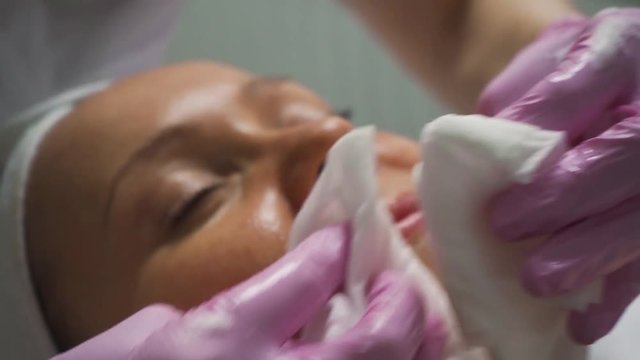 A beautician in a luxury spa salon washes her face with wipes in pink gloves before getting a facial massage for tonus and braces.