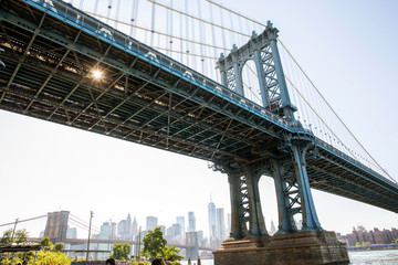 A view from below of the Manhattan Bridge on the Brooklyn waterfront with the city of New York in the background.