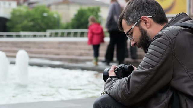 Male bearded tourist with camera takes a video in the park near fountain, blogger takes vlog