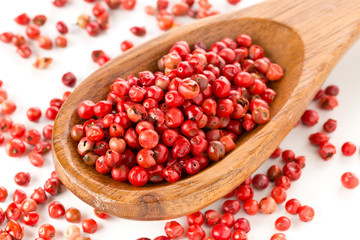 Pink or rose brazilian red peppercorns (schinus terebinthifolius) in wooden spoon over white
