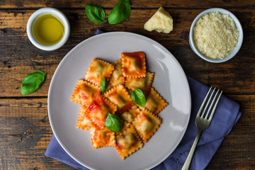 Ravioli stuffed pasta with tomato sauce and basil against dark wooden background