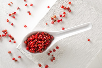 Pink or rose brazilian red peppercorns (schinus terebinthifolius) in white spoon on rustic white wooden table background