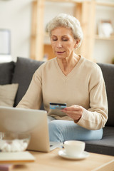 Warm toned portrait of modern senior woman shopping online or paying taxes holding credit card while using laptop at home, copy space