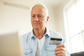 Warm toned portrait of modern senior man shopping online or paying taxes holding credit card while using laptop at home, copy space
