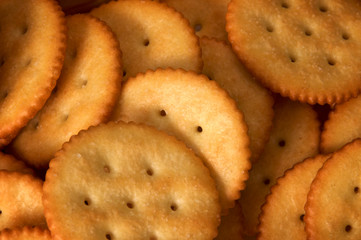 Close up of pile of golden brown butter crackers showing salt, holes, and ridges.