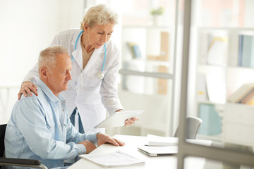 Fototapeta premium Portrait of female doctor using digital tablet while consulting elderly man, copy space