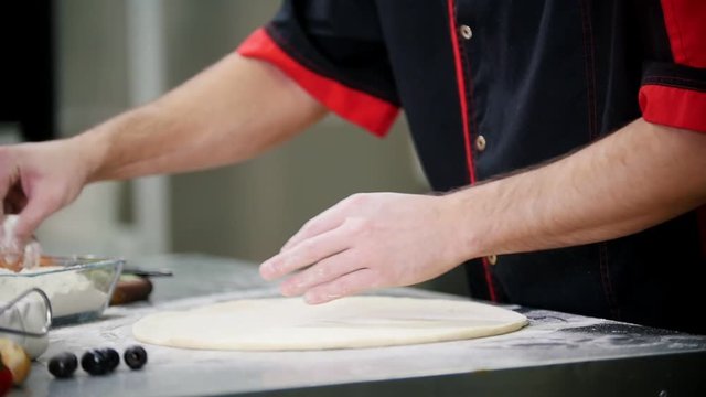 Restaurant kitchen. A man preparing a dough for the pizza. Adding extra flour on the dough