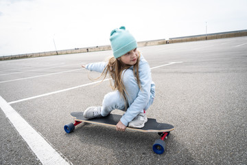 Street sports: A girl in a blue sweater and cap quickly rolls on a longboard. © Aboltin