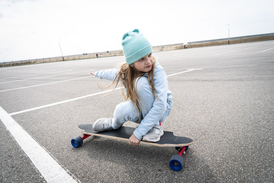 Street sports: A girl in a blue sweater and cap quickly rolls on a longboard.