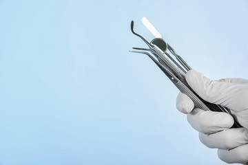 Dentist holding professional tools on light background, closeup. Space for text